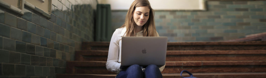 Een student op de trappen van de school, met een Mac op haar schoot